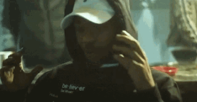 a man wearing a hoodie and a hat is talking on a cell phone .