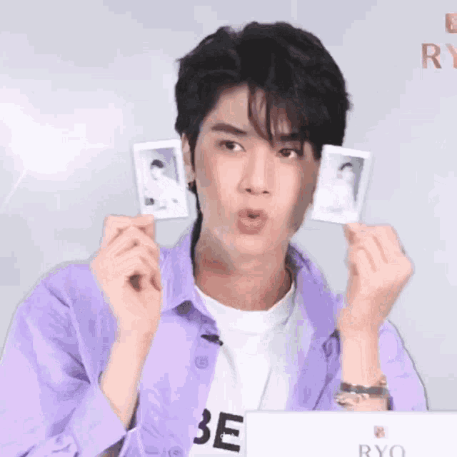 a man in a purple shirt is holding two polaroid pictures in his hands and making a funny face .