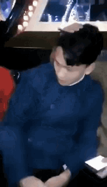 a man in a blue sweater is sitting in a chair with his hands folded