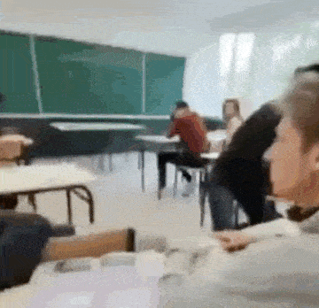 a group of people are sitting at tables in a classroom with a green board .