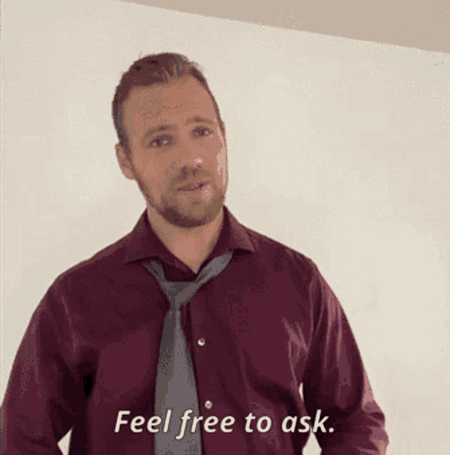 a man in a maroon shirt and tie is standing in front of a white wall and says feel free to ask .