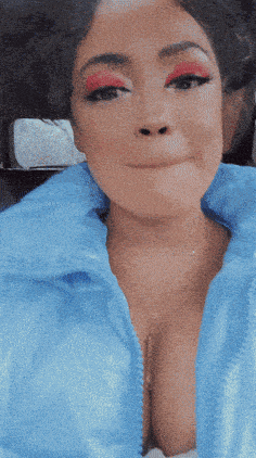 a woman wearing a blue jacket and red eye shadow is making a face