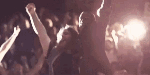 a crowd of people are dancing in a dark room with their arms in the air .