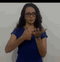 a woman wearing glasses and a blue shirt is making a hand gesture .