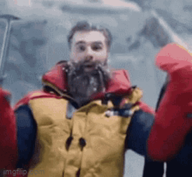 a man with a beard wearing a yellow jacket and red gloves is standing in the snow .