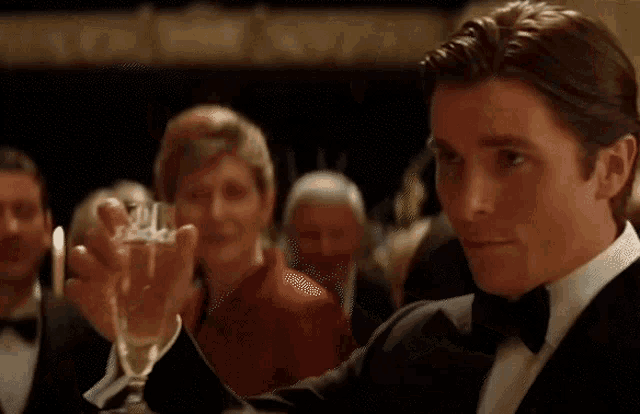 a man in a tuxedo and bow tie is holding a glass of champagne .