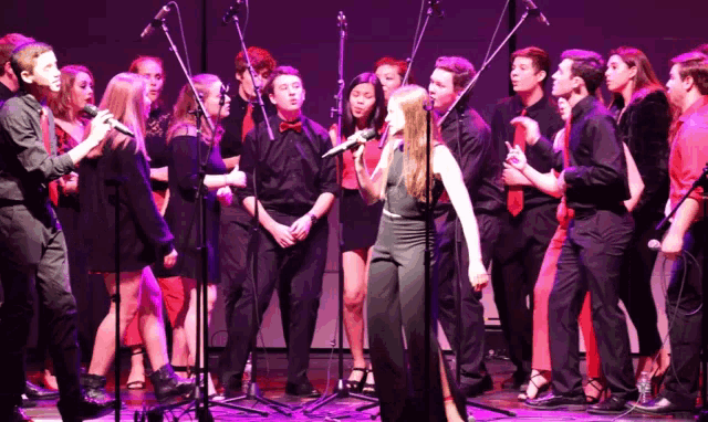 a group of young people singing into microphones on stage