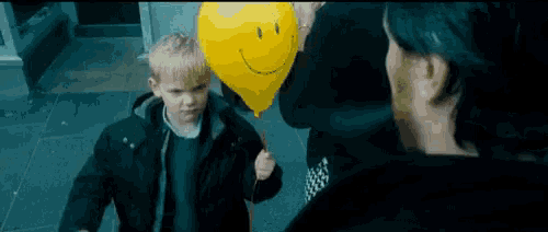 a young boy is holding a yellow balloon with a smiley face on it