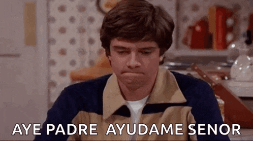 a man is sitting in a kitchen with his mouth open and the words aye padre ayudame senor written on the screen .