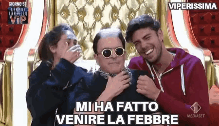 a man wearing sunglasses and a scarf around his neck is surrounded by two other men and a woman laughing .