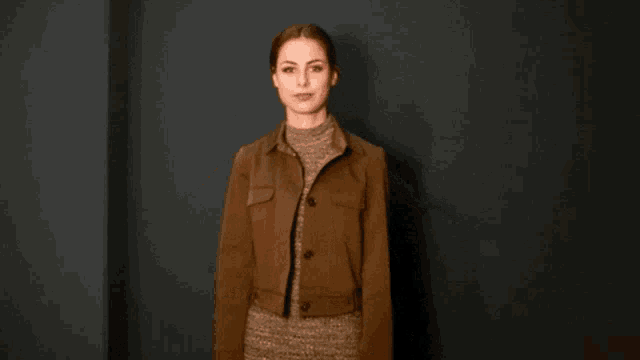 a woman in a brown jacket is giving a thumbs up sign
