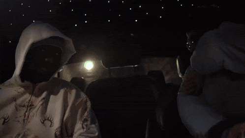 a man wearing a white hoodie and a mask is sitting in a dark room