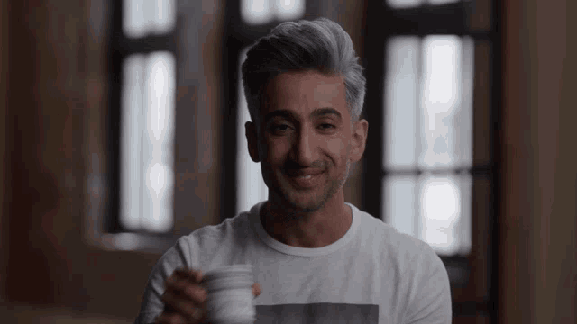 a man in a white shirt is smiling and holding a cup of coffee