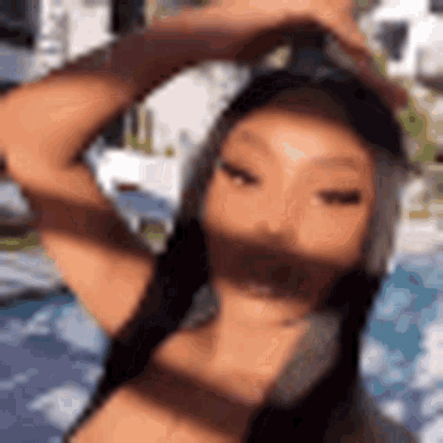 a woman in a bikini is standing in front of a pool with her hand on her head .