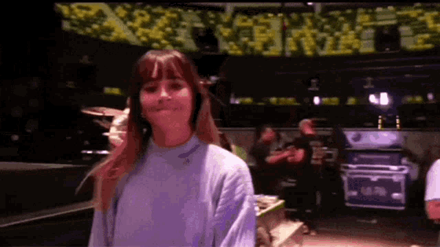 a woman in a purple sweater is smiling in front of a crowd of people .