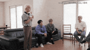 a group of young men are gathered in a living room and one of them is holding a microphone in his hand