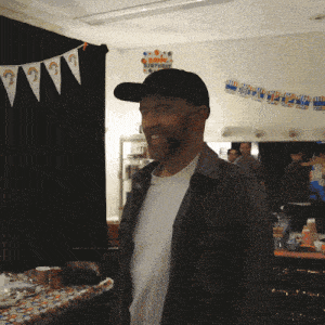 a man wearing a hat stands in front of a birthday banner