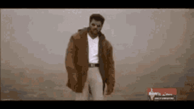 a man in a brown jacket and white shirt is standing in a field .