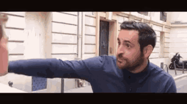 a man in a blue shirt is giving a high five to another man on a street .