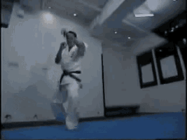a man in a karate uniform is jumping in the air in a room .