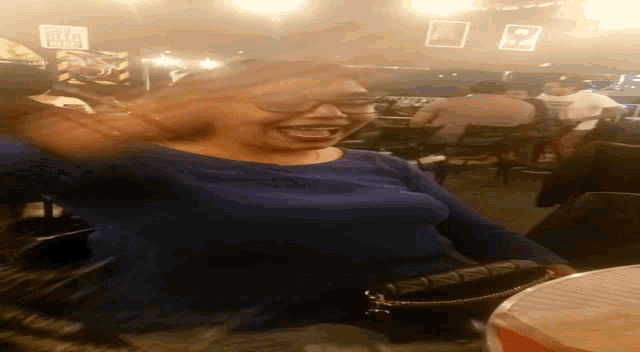 a woman in a blue shirt is laughing in a restaurant with a sign that says ' i love you ' on it