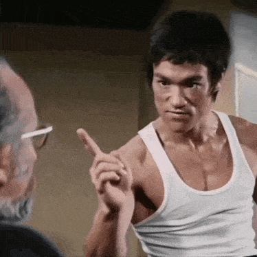 a man in a white tank top is pointing his finger at another man