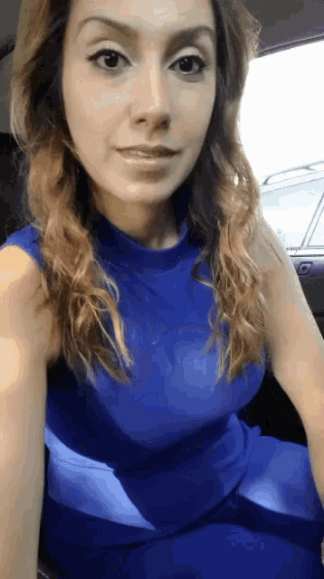 a woman in a blue dress sits in a car