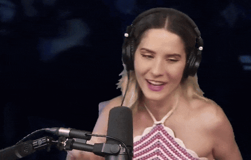a woman wearing headphones stands in front of a microphone and smiles