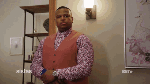 a man in a floral shirt and vest is standing in front of a wall with a picture of a peacock on it