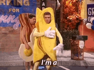 a man in a banana costume is giving a thumbs up while walking down a street .