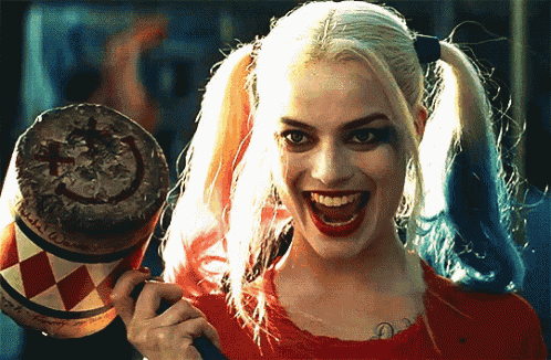 a woman in a harley quinn costume is holding a bat and smiling