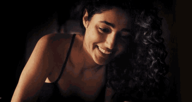 a woman with curly hair wearing a black tank top is smiling