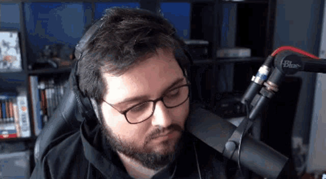 a man wearing glasses and headphones stands in front of a blue microphones