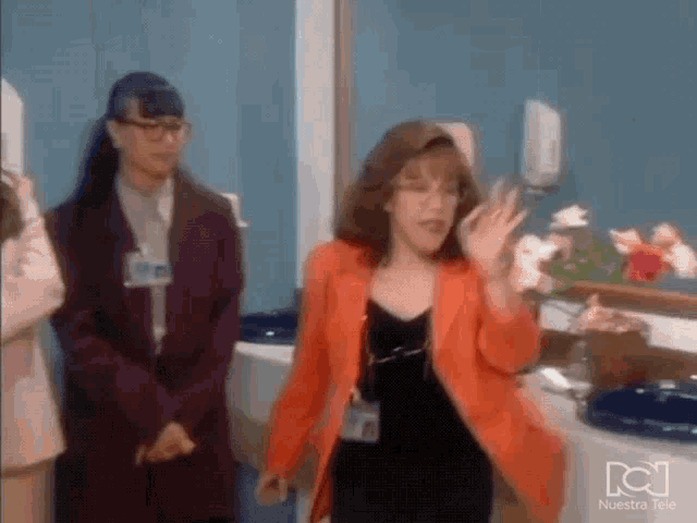 a woman in an orange jacket is standing in front of a sink .