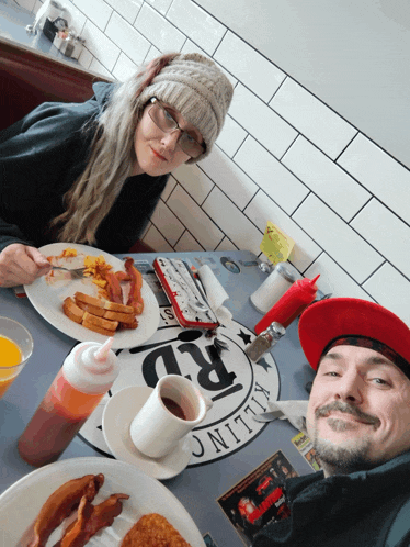 a man and a woman are sitting at a table with plates of food and a sign that says killing rd