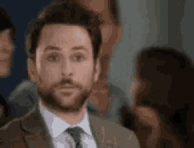 a man with a beard is wearing a suit and tie and looking at the camera .