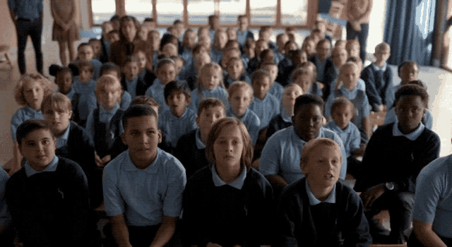a large group of children in school uniforms are sitting in a room