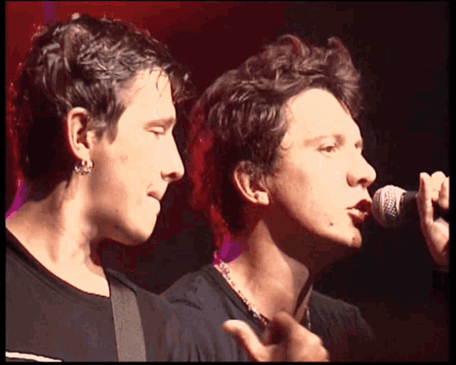 a man singing into a microphone next to another man with earrings