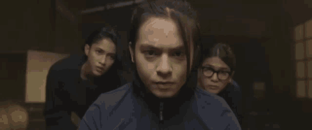 a man with long hair looks at the camera while two other people look on