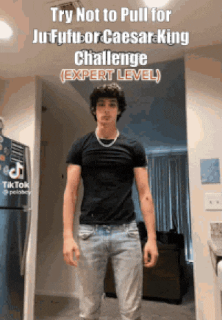 a young man in a black shirt and jeans is standing in front of a refrigerator in a room .