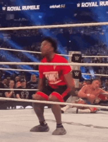 a wrestler in a red shirt is squatting in a wrestling ring .