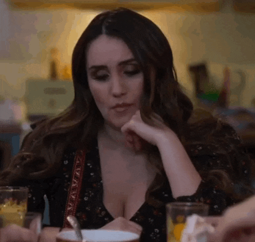 a woman in a plunging neckline is sitting at a table with a cup of coffee .