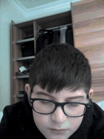 a young man wearing glasses looks down at something