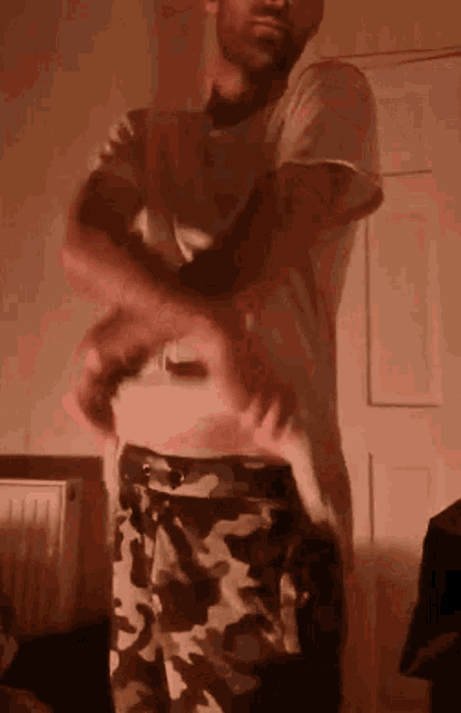 a man in a white shirt and camo shorts is standing in a room .