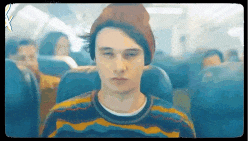 a young man wearing a beanie and a sweater is sitting on an airplane