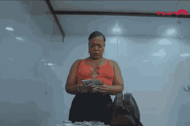 a woman in an orange tank top is holding a bunch of money in her hands .