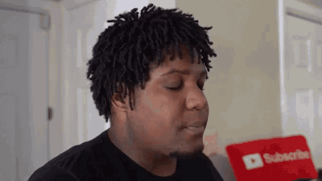 a man with dreadlocks is sitting in front of a red pillow that says subscribe on it .