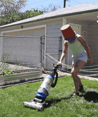a woman wearing a bucket on her head is vacuuming the grass