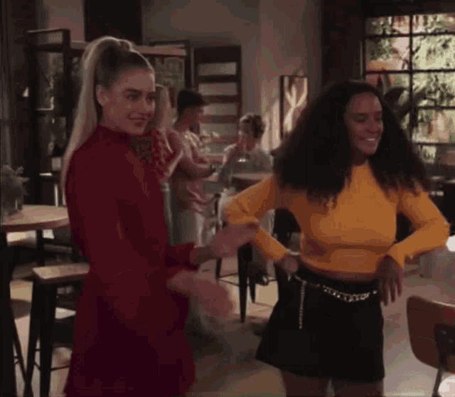 two women are dancing in a restaurant and one is wearing a yellow top