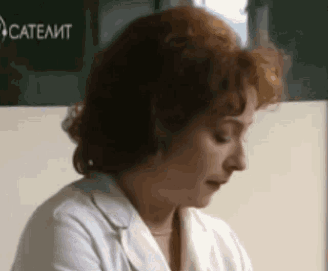 a woman in a white lab coat looks down at something in front of a sign that says catelit